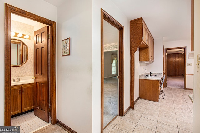 hall featuring light tile patterned floors, baseboards, and a sink