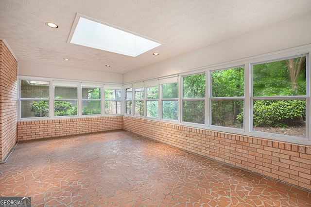 unfurnished sunroom with a textured ceiling, brick wall, recessed lighting, and a skylight