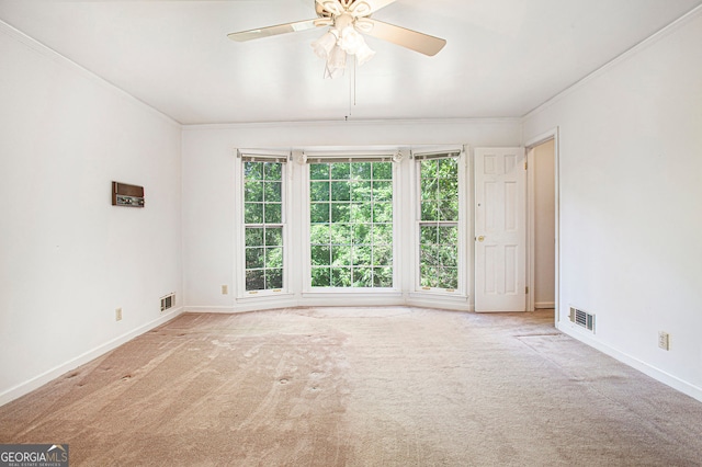 carpeted empty room featuring baseboards, ornamental molding, a ceiling fan, and visible vents