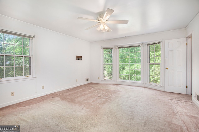carpeted empty room with visible vents, ornamental molding, baseboards, and ceiling fan