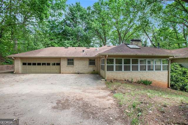 ranch-style house with brick siding, an attached garage, a chimney, and a sunroom