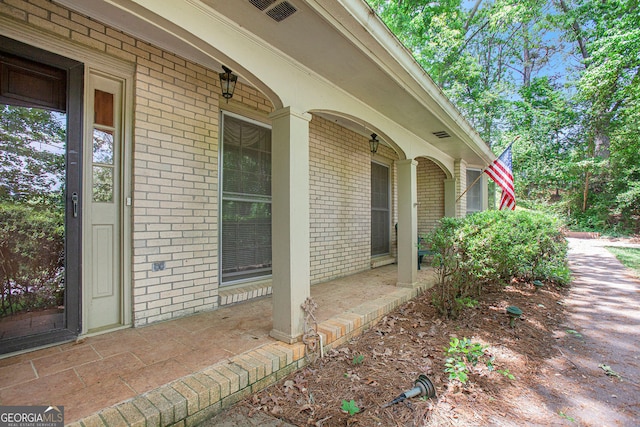 doorway to property featuring a porch and brick siding
