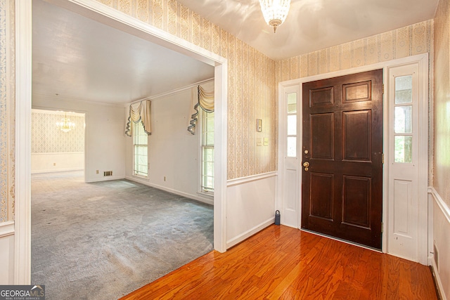 foyer entrance featuring baseboards, wood finished floors, a chandelier, and wallpapered walls