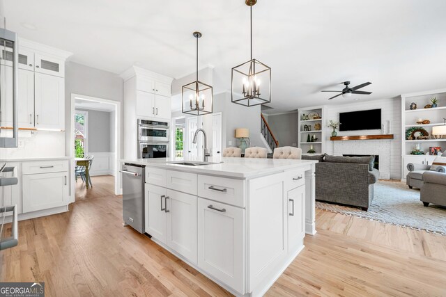 kitchen with appliances with stainless steel finishes, a sink, light wood-style floors, light countertops, and ceiling fan with notable chandelier
