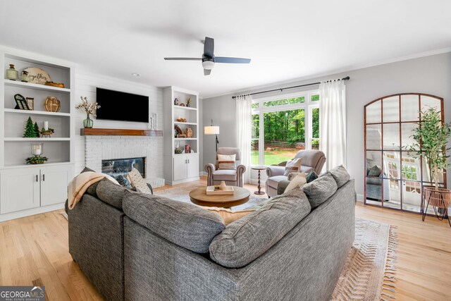 living room with ornamental molding, a ceiling fan, a brick fireplace, and light wood-style flooring