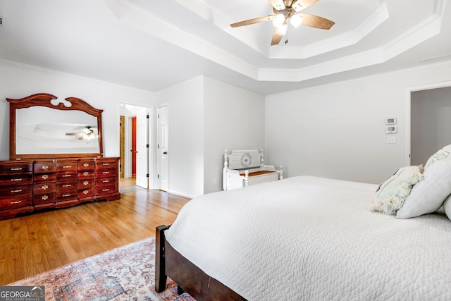 bedroom with ceiling fan, a raised ceiling, ornamental molding, and light wood-style flooring