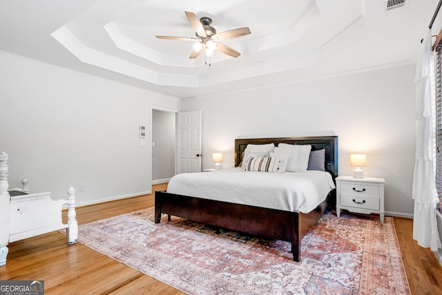 bedroom with a ceiling fan, ornamental molding, wood finished floors, and a raised ceiling