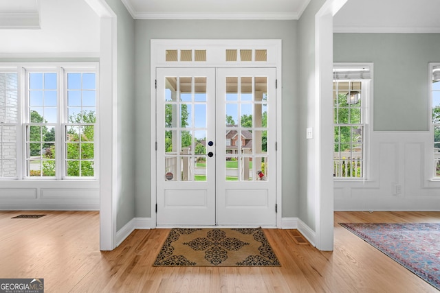 foyer entrance with crown molding, french doors, light wood finished floors, and a healthy amount of sunlight