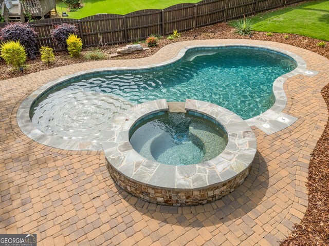 view of pool featuring fence and a pool with connected hot tub