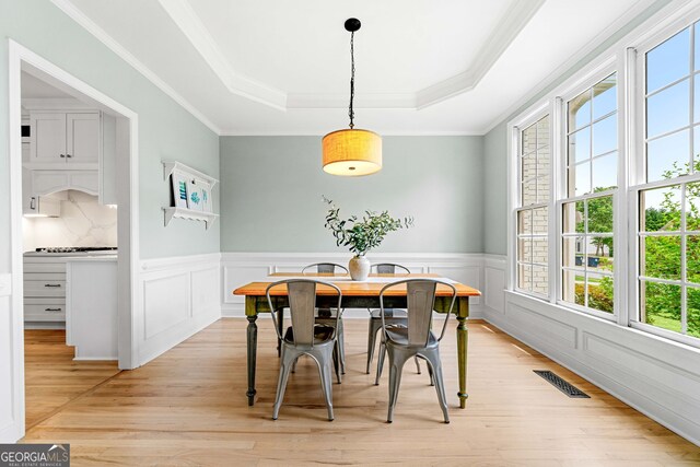 dining room featuring crown molding, a wainscoted wall, light wood-type flooring, a tray ceiling, and visible vents
