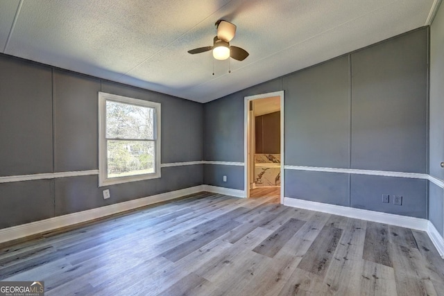 spare room with ceiling fan, a textured ceiling, wood finished floors, baseboards, and lofted ceiling