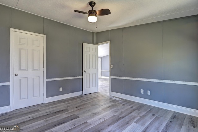 unfurnished bedroom featuring wood finished floors, a ceiling fan, baseboards, and a decorative wall