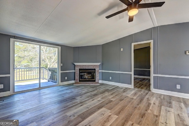 unfurnished living room with a fireplace, a ceiling fan, baseboards, wood finished floors, and lofted ceiling