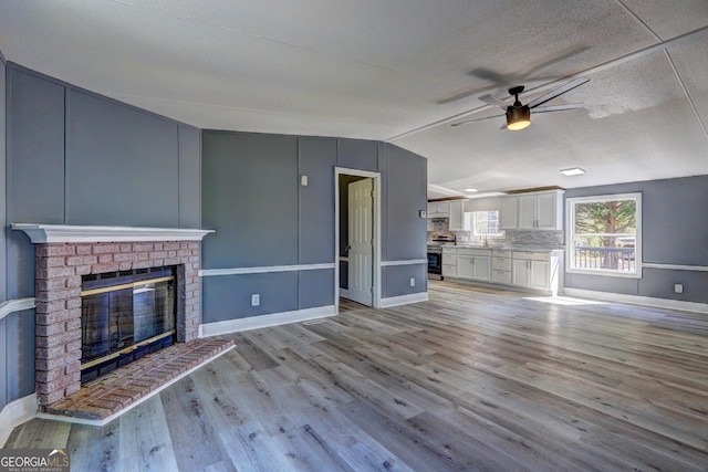 unfurnished living room featuring baseboards, a ceiling fan, lofted ceiling, and light wood-type flooring