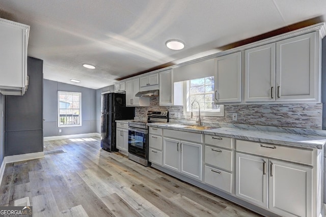 kitchen featuring a sink, stainless steel range with electric stovetop, freestanding refrigerator, lofted ceiling, and under cabinet range hood