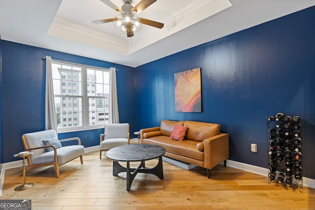 living area featuring crown molding, a raised ceiling, a ceiling fan, baseboards, and light wood-type flooring