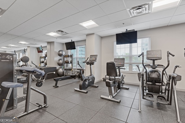 workout area featuring visible vents, baseboards, a drop ceiling, and a healthy amount of sunlight
