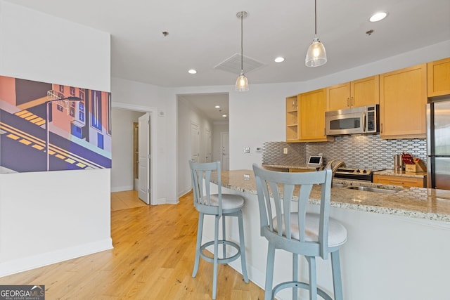 kitchen with light stone countertops, light wood-type flooring, tasteful backsplash, hanging light fixtures, and stainless steel appliances