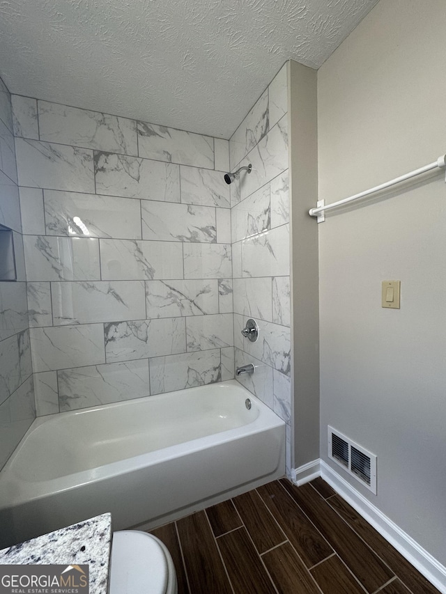 full bath with visible vents, baseboards, bathtub / shower combination, wood finish floors, and a textured ceiling