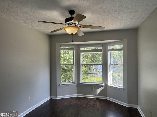 empty room with ceiling fan, a textured ceiling, visible vents, baseboards, and dark wood-style floors