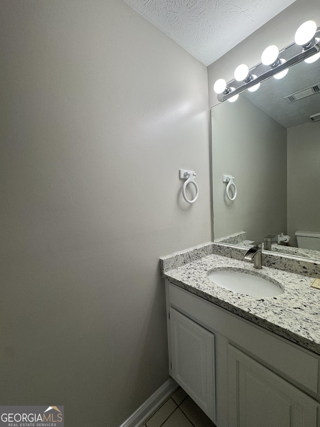 half bath with visible vents, tile patterned flooring, vanity, toilet, and baseboards