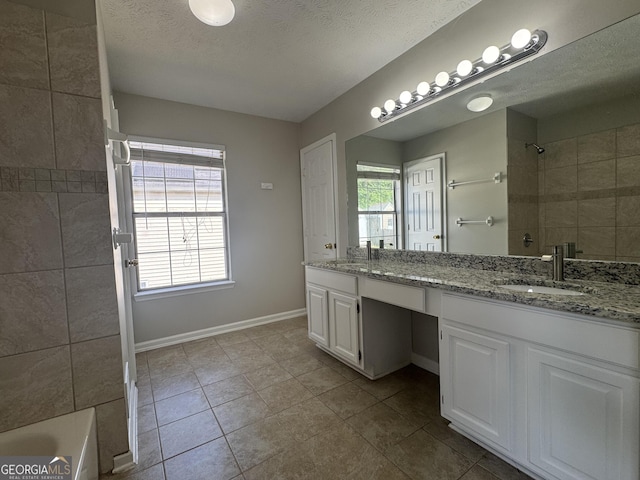 bathroom featuring a tile shower, a sink, double vanity, a textured ceiling, and baseboards