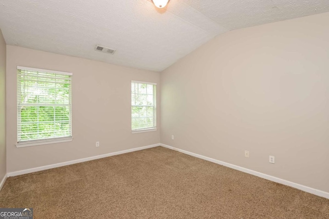empty room with a textured ceiling, carpet, baseboards, vaulted ceiling, and visible vents