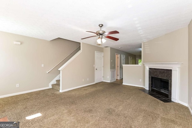 unfurnished living room with ceiling fan, carpet floors, a textured ceiling, baseboards, and stairway