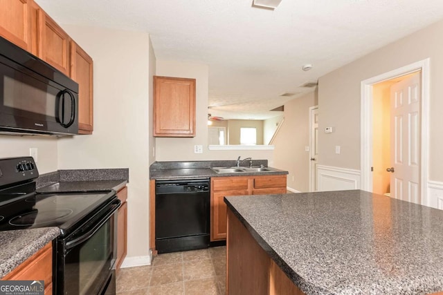 kitchen with ceiling fan, dark countertops, brown cabinets, a sink, and black appliances
