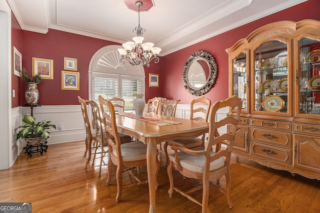 dining area featuring crown molding, a chandelier, light wood-type flooring, and a wainscoted wall