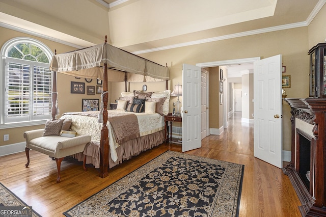 bedroom with crown molding, baseboards, wood finished floors, and a fireplace