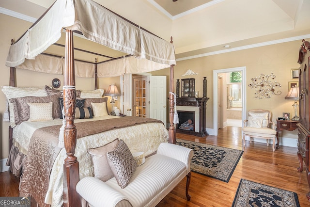 bedroom with crown molding, a fireplace, wood finished floors, baseboards, and ensuite bathroom