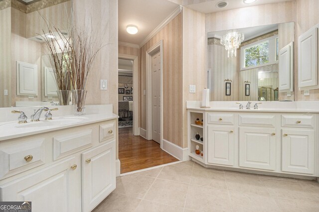 ensuite bathroom featuring crown molding, an inviting chandelier, a sink, baseboards, and two vanities