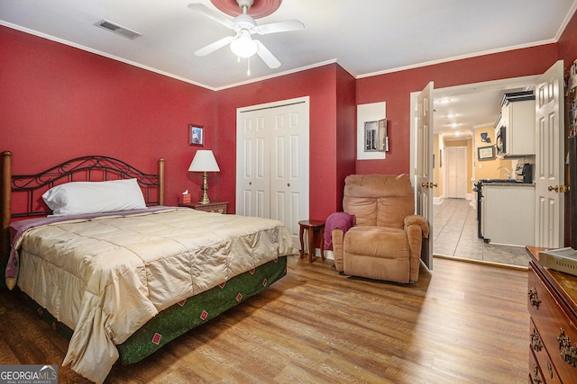 bedroom featuring crown molding, light wood-style flooring, a ceiling fan, visible vents, and a closet