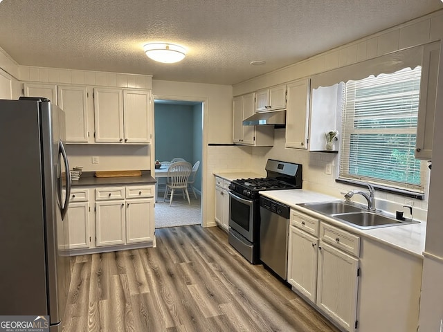 kitchen featuring a textured ceiling, appliances with stainless steel finishes, a sink, light wood finished floors, and under cabinet range hood