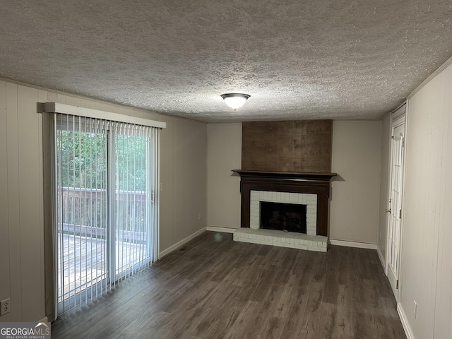 unfurnished living room featuring a brick fireplace, a textured ceiling, dark wood finished floors, and baseboards