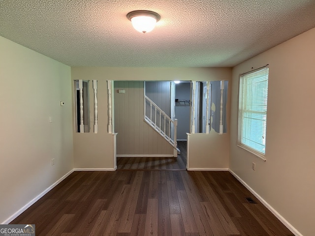 unfurnished room with visible vents, stairs, wood finished floors, baseboards, and a textured ceiling