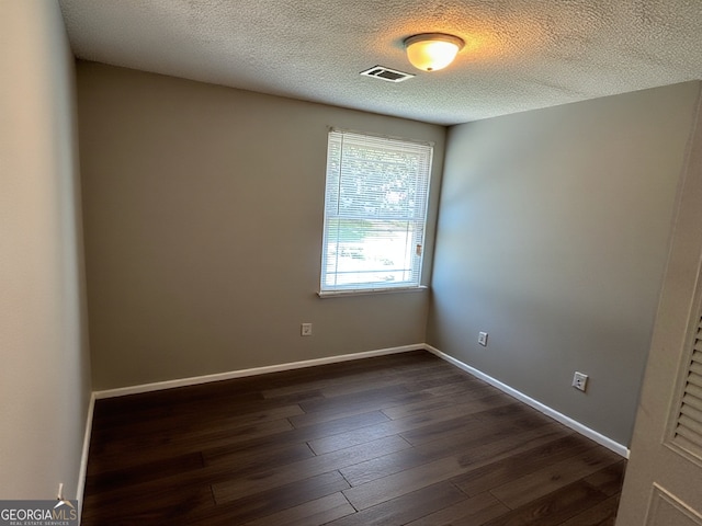 spare room with baseboards, dark wood-style floors, a textured ceiling, and visible vents