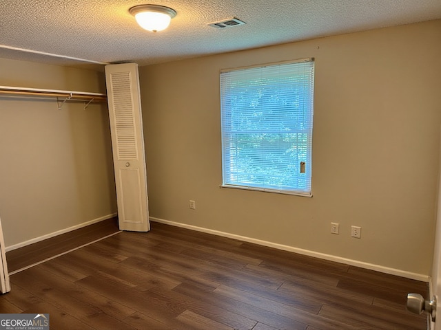 unfurnished bedroom with a textured ceiling, visible vents, baseboards, a closet, and dark wood-style floors