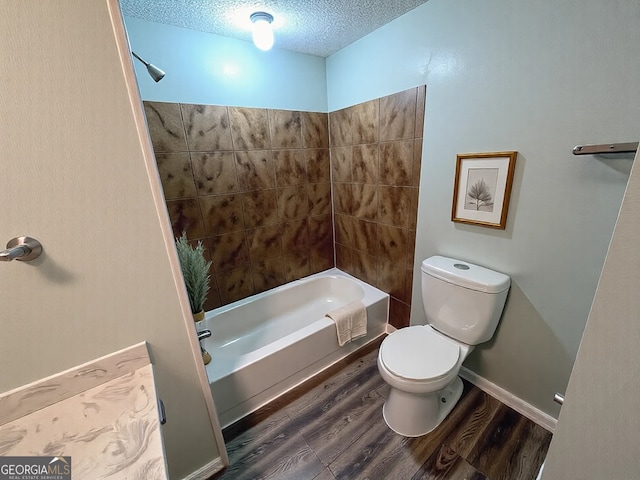 bathroom with a textured ceiling, wood finished floors, baseboards, toilet, and washtub / shower combination