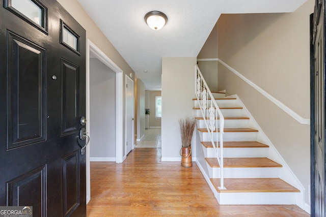 foyer entrance featuring light wood-type flooring, stairs, and baseboards