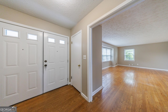 entrance foyer with light wood-type flooring, a textured ceiling, and baseboards