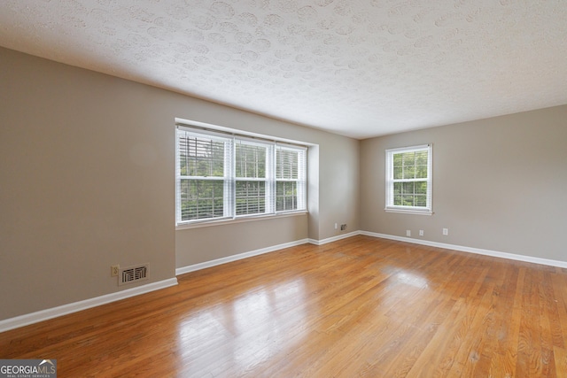 unfurnished room with visible vents, a textured ceiling, light wood-style flooring, and baseboards