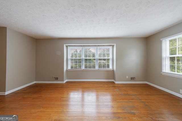 empty room with light wood-style floors, a textured ceiling, baseboards, and visible vents