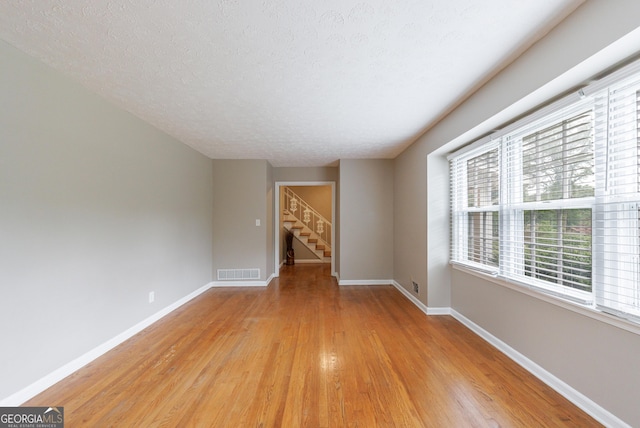 spare room featuring visible vents, baseboards, stairway, light wood-type flooring, and a textured ceiling