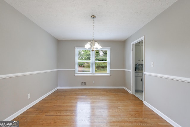 unfurnished dining area with visible vents, baseboards, a textured ceiling, light wood-style flooring, and a notable chandelier