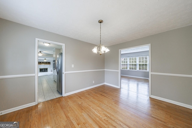 unfurnished dining area with baseboards, an inviting chandelier, light wood-style flooring, and a fireplace