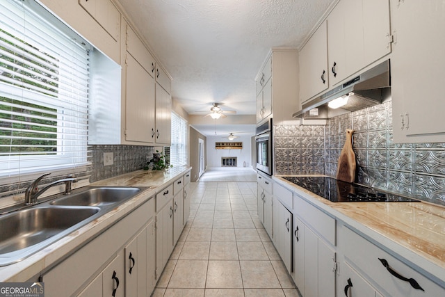 kitchen with ceiling fan, a sink, stainless steel oven, light tile patterned floors, and under cabinet range hood