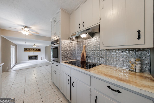 kitchen featuring oven, black electric stovetop, under cabinet range hood, a ceiling fan, and light tile patterned floors