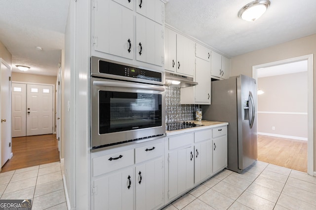 kitchen featuring a textured ceiling, under cabinet range hood, tasteful backsplash, light tile patterned floors, and stainless steel appliances
